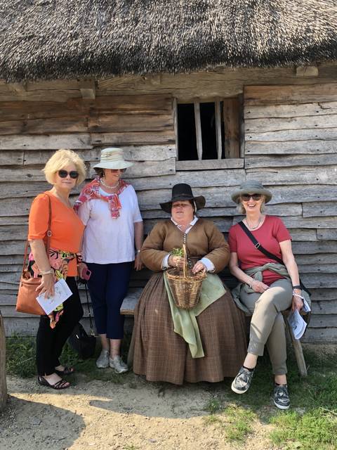 People in historical attire sitting by a wooden house.