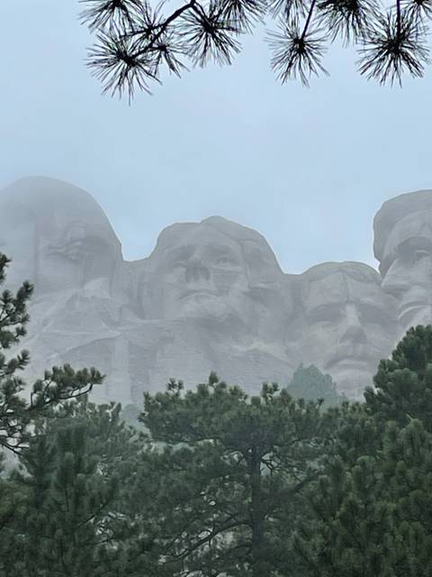       Mount Rushmore partially obscured by fog and trees.
  