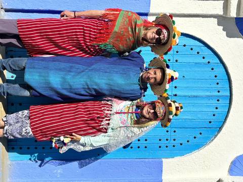       Three people in colorful traditional attire in front of a blue door.
  