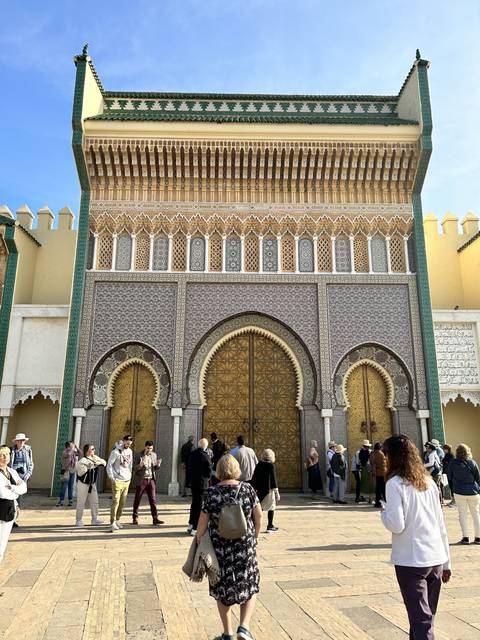       People gathered outside a grand ornamental gate.
  