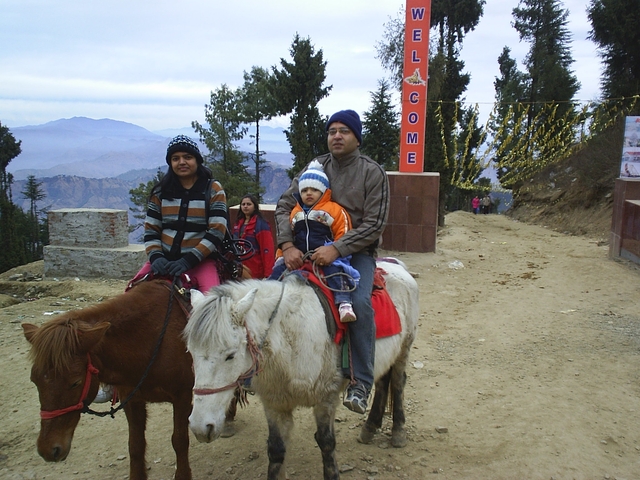       Family riding horses on a mountain path under a cloudy sky.
  