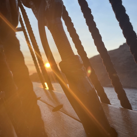       Sunset view through ship ropes with a distant rock formation.
  