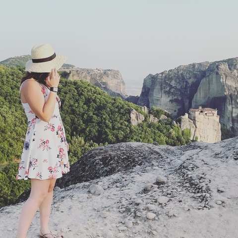       Woman in a floral dress admiring a mountainous landscape with monasteries.
  