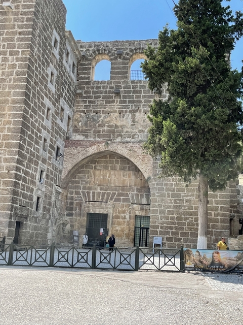       Stone building with an arched entrance and a tree.
  
