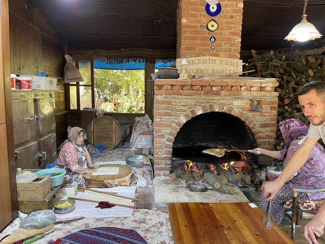       People preparing traditional food near a brick oven.
  