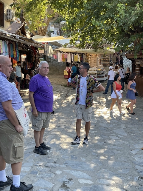       People walking through a market area with stalls and items displayed.
  
