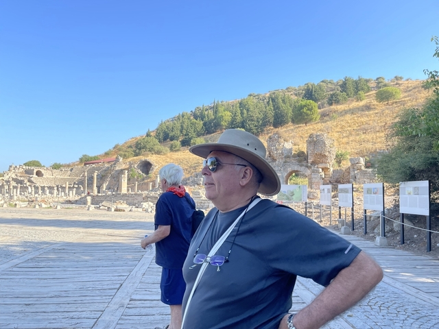      Two people standing near ancient ruins with a scenic backdrop.
  