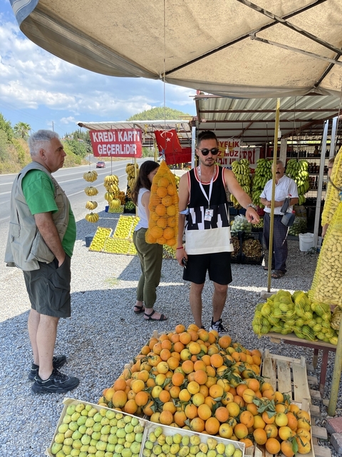       People at a roadside fruit market with various produce.
  