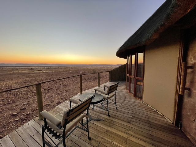       Outdoor view from a deck with chairs facing a sunset landscape.
  