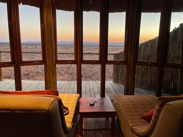       Interior view of a room with large windows showing a sunset over a desert landscape.
  