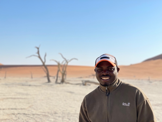       Person smiling with desert landscape and dead trees in the background.
  