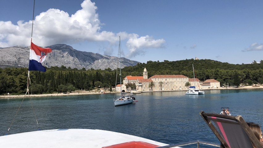       View from a boat, showing a scenic coastal area with hills and a Croatian flag.
  