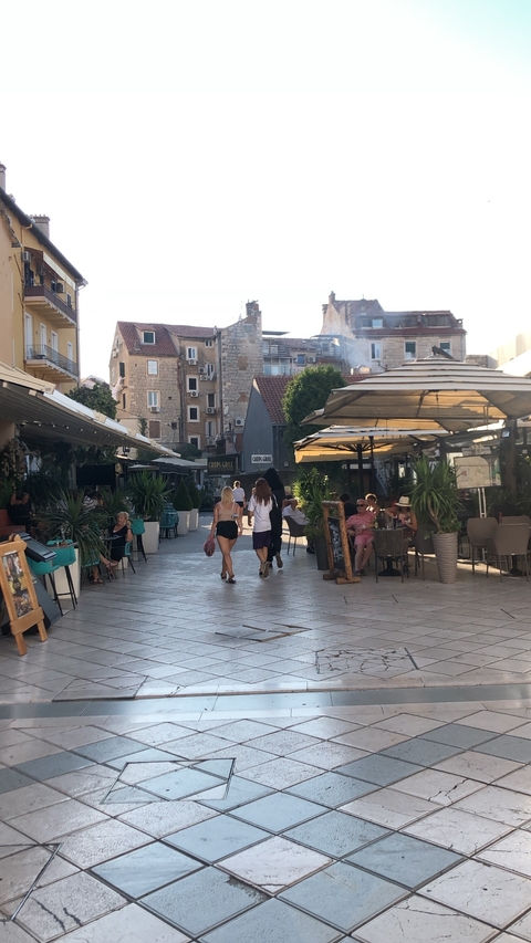       People walking in a lively outdoor cafe area.
  