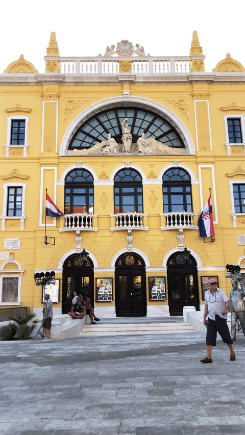       Yellow building with arch windows and Croatian flags.
  