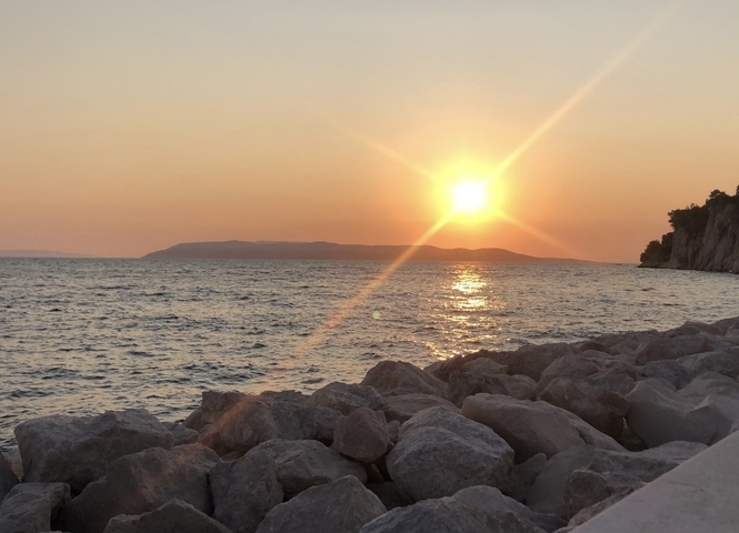       Sunset over the sea viewed from a rocky shore.
  