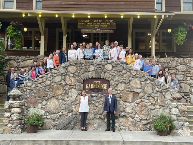 Large group of people posing in front of a lodge with a sign.