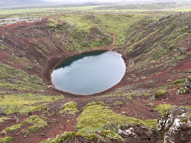Circular crater lake surrounded by red volcanic soil.