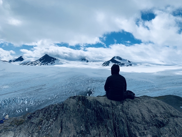       Person sitting on a rock overlooking a snowy mountain range.
  