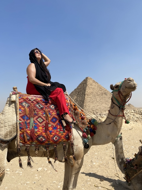       Person on a camel with pyramids in the background.
  
