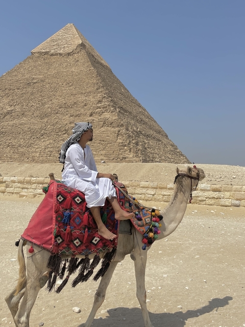 Person riding a camel near the pyramids.
