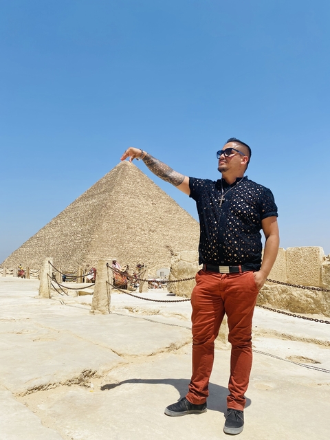       Man pretending to hold the tip of a pyramid.
  