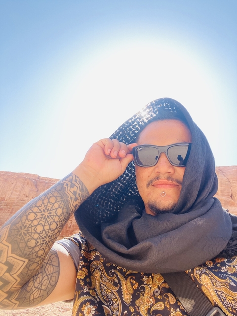       A person in sunglasses posing in a desert landscape.
  