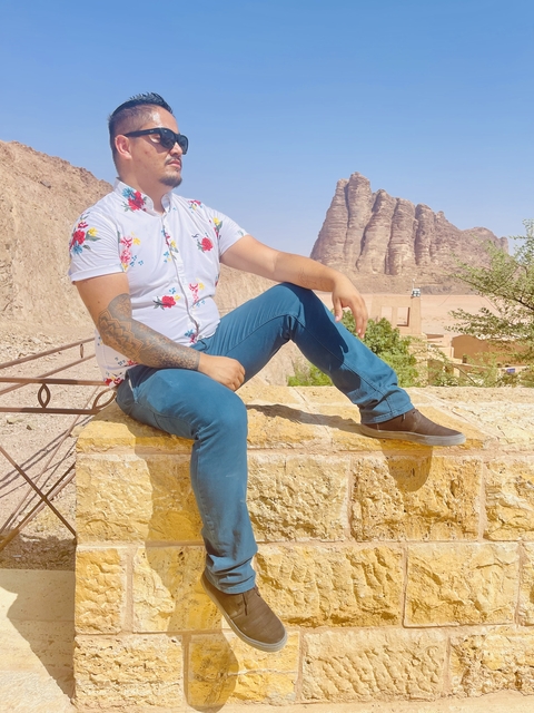       A man sitting on a stone wall with mountains in the background.
  