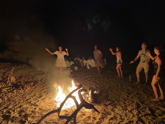       Group of people dancing around a campfire at night.
  