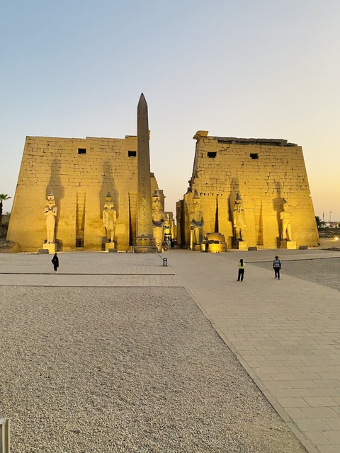       An ancient Egyptian gate with statues and people around.
  