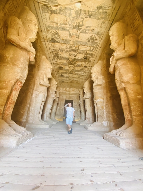       Man walking inside a temple with large statues and columns.
  