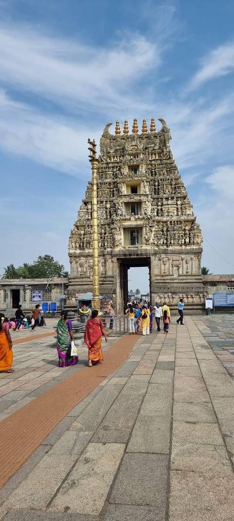       Ornate temple gateway with people walking by.
  