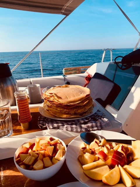 Stack of pancakes on a boat with honey and coffee.