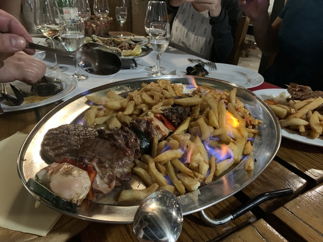 Flaming platter of food at a dining table.