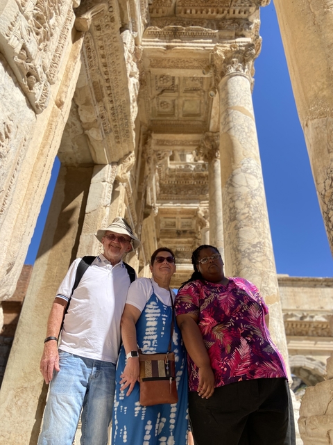       Three people in front of ancient ruins with columns.
  