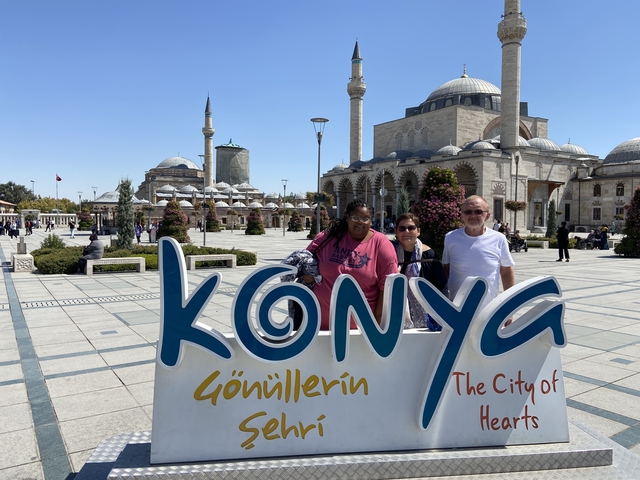       Three people in front of Konya city sign and mosque.
  