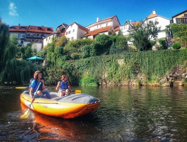 Two people kayaking in a river with houses on the riverbank.