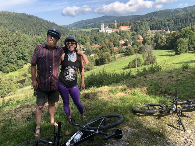 Two people with bikes overlooking a valley with forest and houses.