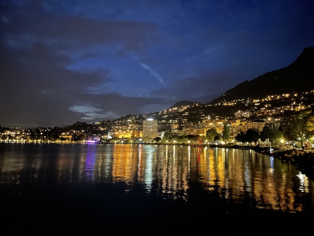 Night cityscape reflected on a lake with illuminated buildings.