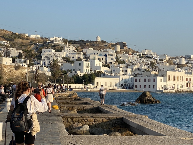       People walking along a waterfront with white houses.
  