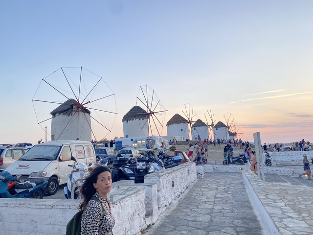       View of multiple windmills with people walking nearby.
  