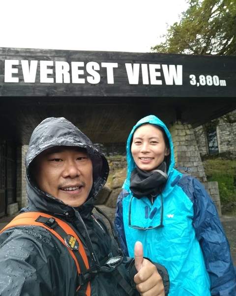 Two people dressed in rain gear in front of a building sign.