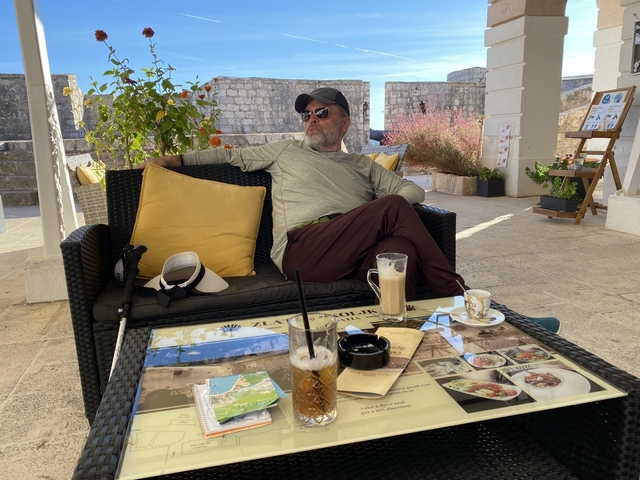 Man seated at an outdoor cafe with drinks on the table.
