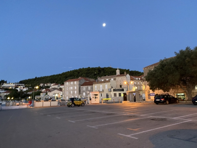 Town square with buildings and a hillside under the moon.