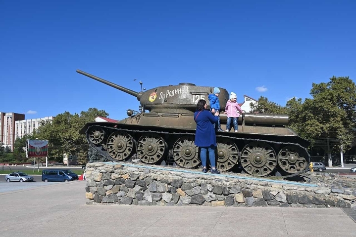       People climbing on a tank monument in a plaza.
  