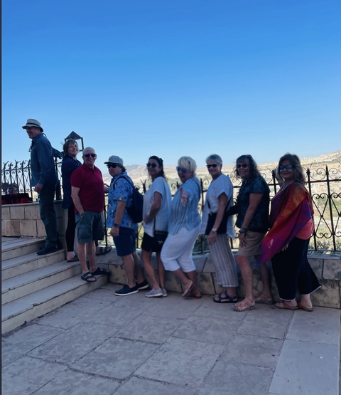       Group of people posing by a fence with a city view.
  