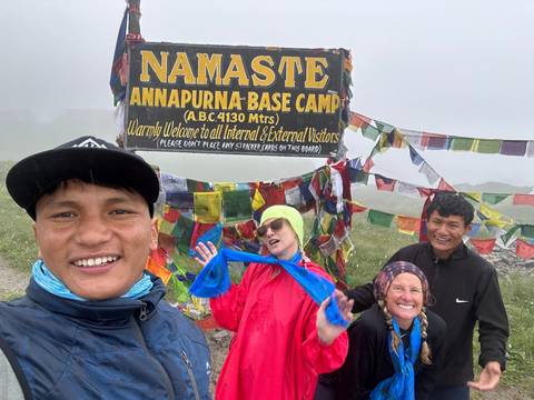       Group of people posing at Annapurna Base Camp with prayer flags in the background.
  