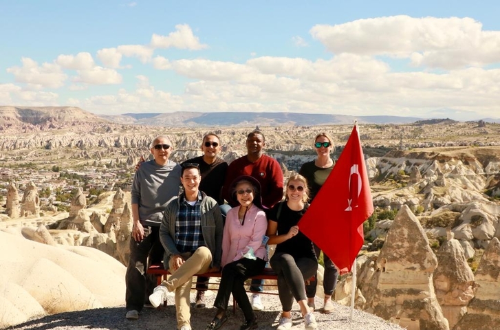       Group of people with a Turkish flag overlooking Cappadocia.
  