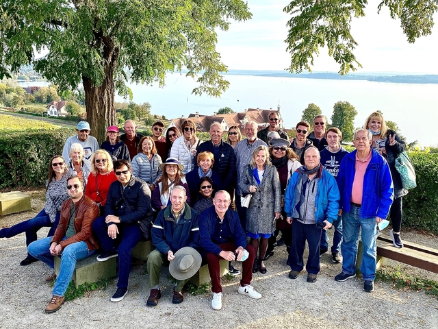 A large group of people posing with a scenic vista of a lake and hills.