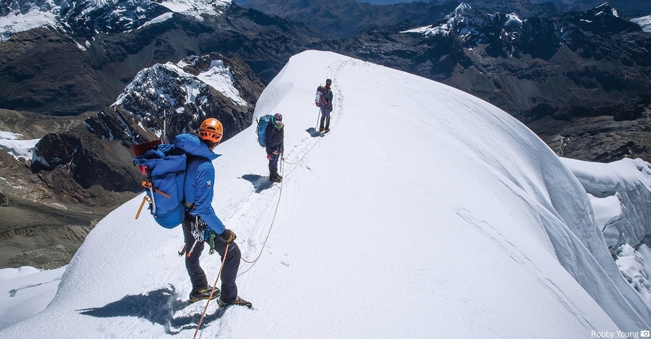       Mountain climbers on a snowy peak with mountains in the background.
  