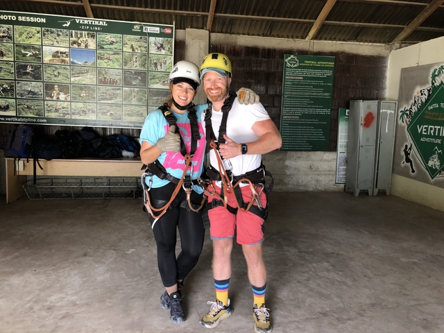       Two people in harnesses posing indoors with adventure gear.
  